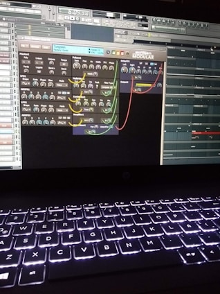 A computer screen displays a digital audio workstation with various audio controls and modules visible. The screen is filled with plugins and mixer settings for music production. Below the screen, a laptop keyboard is visible, illuminated by a backlight.