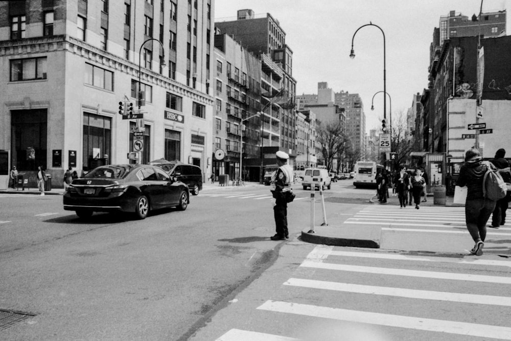 grayscale photograph of man standing in middle of street beside vehicle