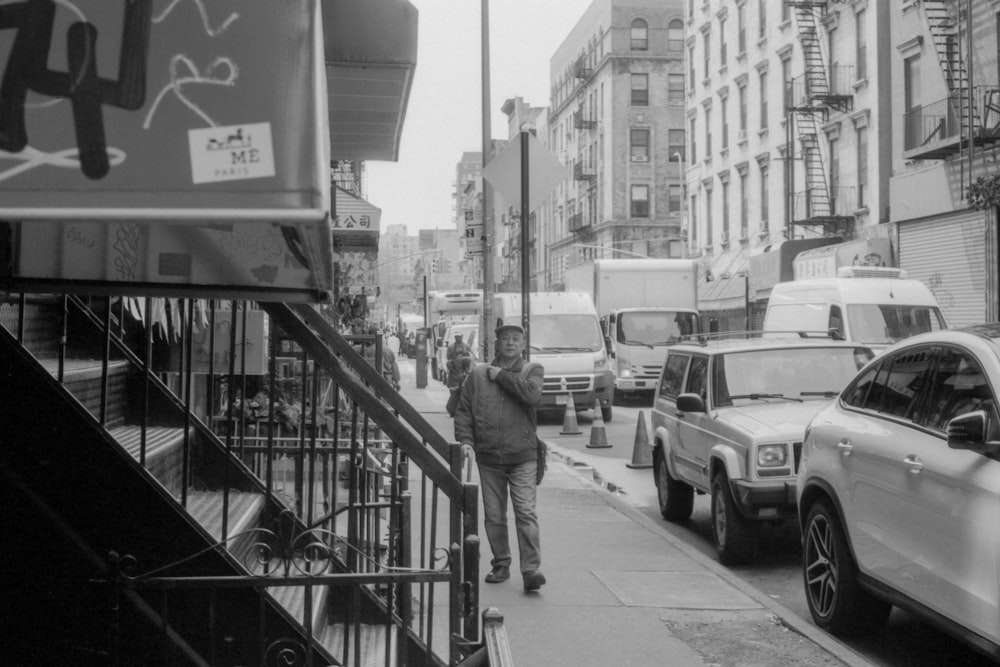 grayscale photography of man walking on street beside vehicles