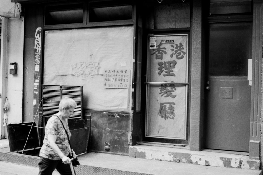 grascale photography of woman walking beside building