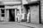 Three individuals in aprons stand and converse near the entrance of a building with closed metal shutters. The scene is urban, likely outside a shop, showcasing a casual interaction between workers during a break.