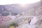 A hiker pausing on a sunlit mountain path overlooking the white village of Mijas with olive groves below.