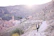 A hiker pausing on a sunlit mountain path overlooking the white village of Mijas with olive groves below.