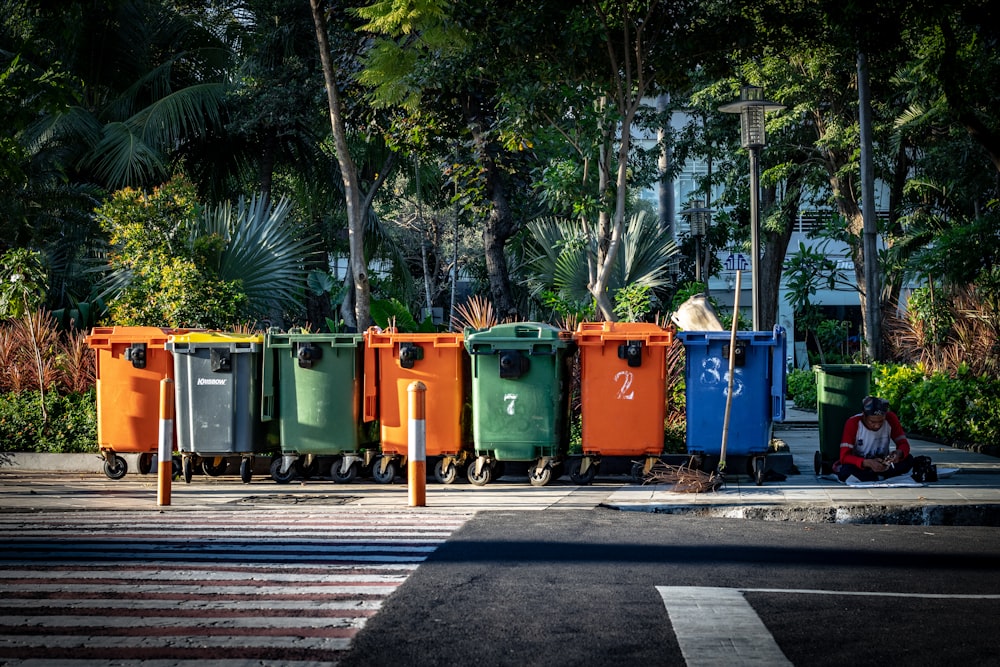 Cubos de basura de colores variados en la acera durante el día