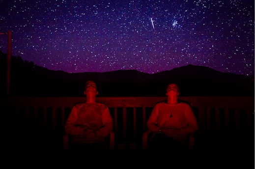 two men sitting under starry sky during nighttime