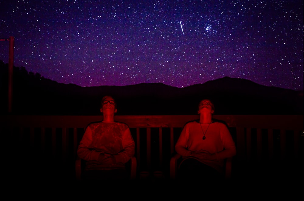 Zwei Männer sitzen nachts unter dem Sternenhimmel