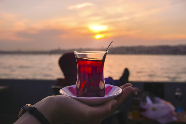 A luxury hotel balcony overlooking a calm ocean at sunset, with a traveler sipping tea.