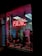A storefront features a prominently displayed neon sign with the word 'PSYCHIC' in bright red. The window is adorned with red string lights and contains various decorative items, including statues and plants. A poster inside provides additional information on psychic services.
