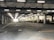 An indoor loading dock area with a large, open space. Fluorescent lights are affixed to the ceiling, illuminating the area. A white delivery truck is parked on the right side near a section with loading bays. The area appears industrial, with exposed concrete floors and columns.