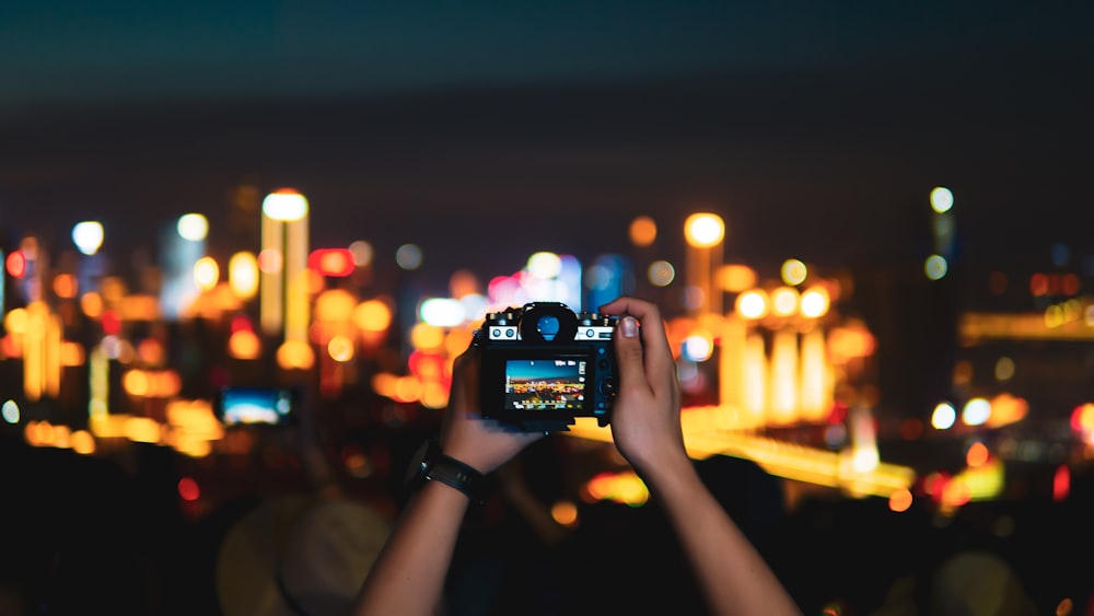 man taking photo of lighted city skyline at night with DSLR camera