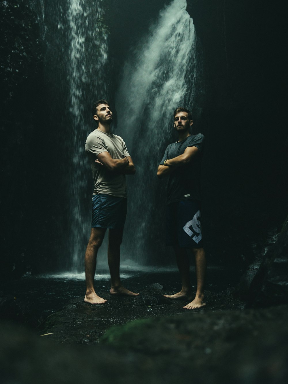 two men standing at bottom of waterfall
