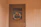 A wooden door set within a paneled wall is adorned with a decorative wreath. The wreath includes a variety of colorful flowers and ribbons, adding a touch of festivity. The light hue of the wood gives a warm and welcoming appearance.