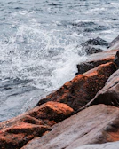 Waves crashing against rocks with a Mastrimersil surfboard standing upright