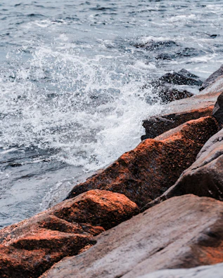 Waves crashing against rocks with a Mastrimersil surfboard standing upright