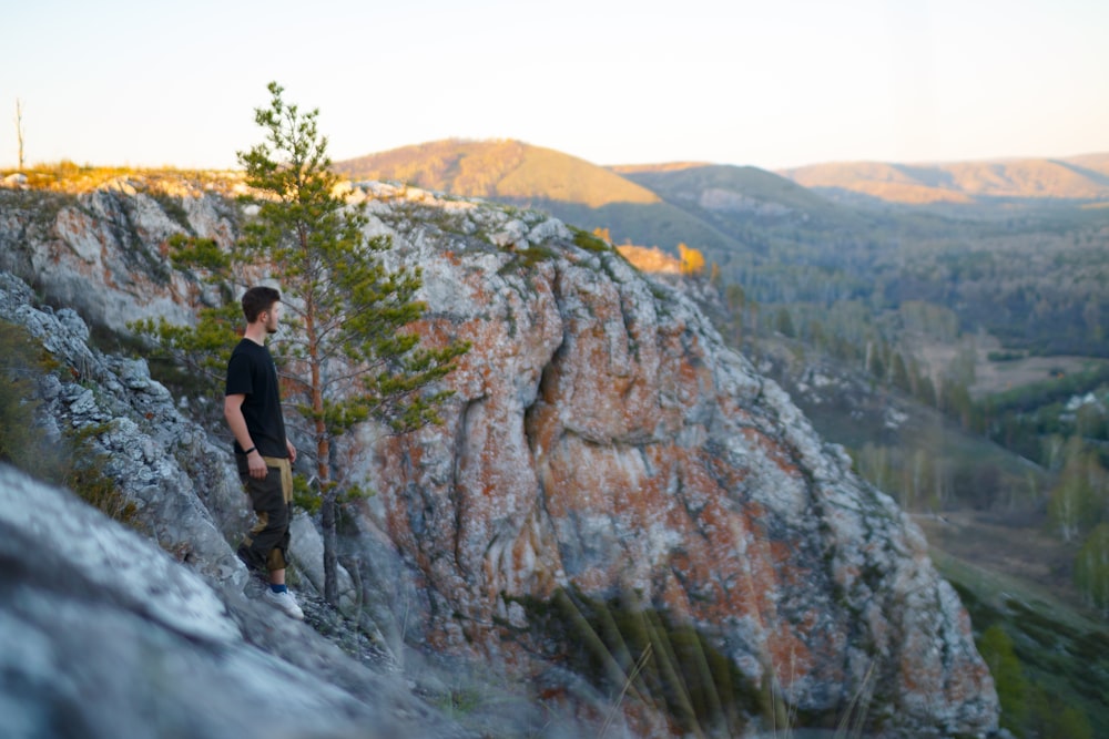 man standing on cliff beside green leafed tree