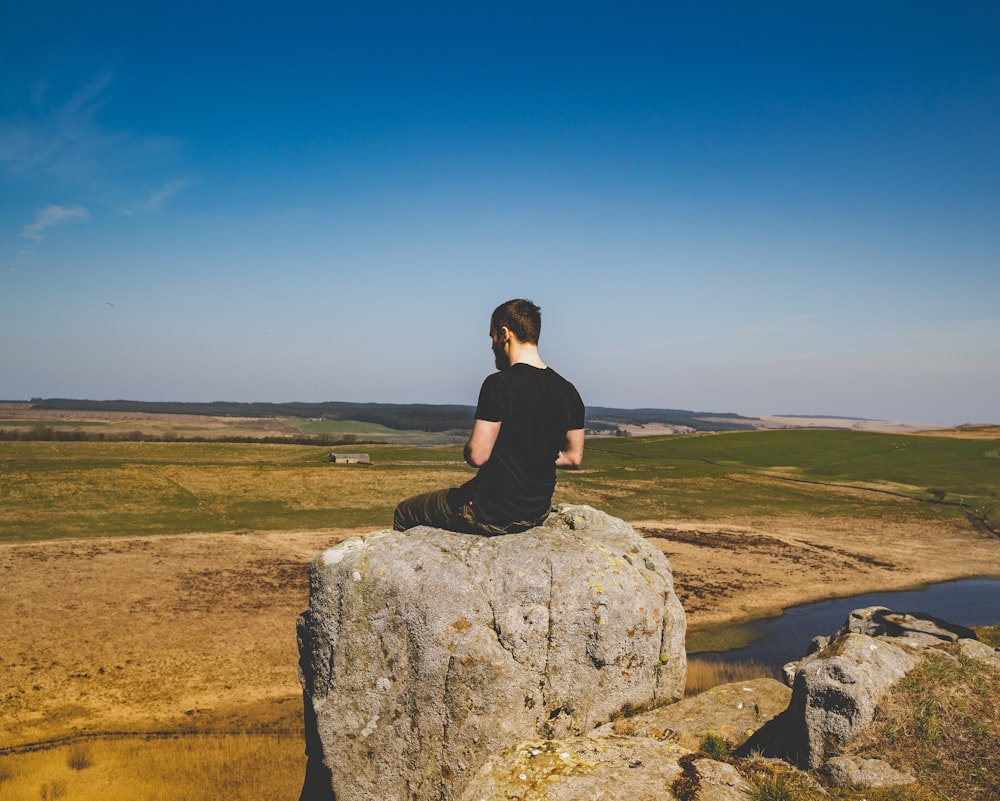 man sitting on rock under blue sky during daytime
