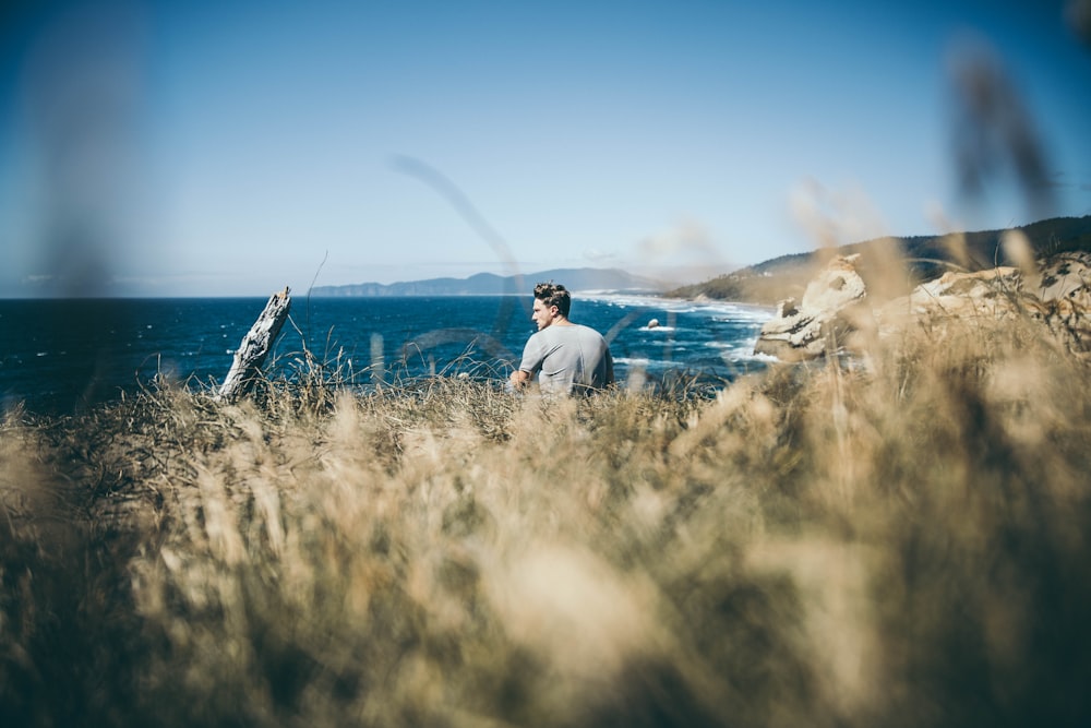 man sitting on a mountain overlooking the ocean