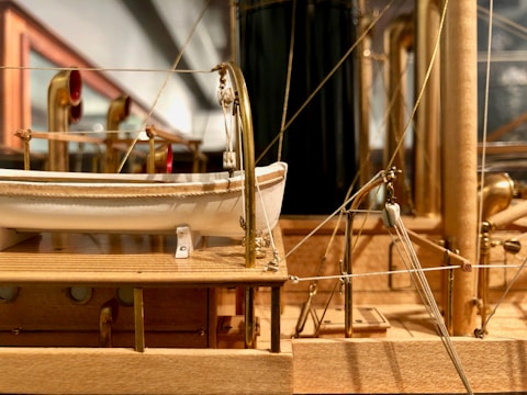 A detailed wooden model of a ship, showcasing lifeboats, brass fittings, and intricate rigging. The craftsmanship highlights realistic textures and precise construction, emphasizing a lifelike representation of a historical vessel.