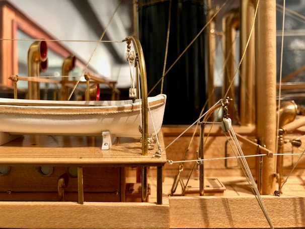 A detailed wooden model of a ship, showcasing lifeboats, brass fittings, and intricate rigging. The craftsmanship highlights realistic textures and precise construction, emphasizing a lifelike representation of a historical vessel.