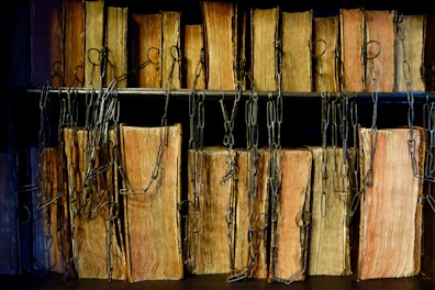 A row of old, leather-bound books is lined up on shelves, secured by metal chains. The books have worn pages and weathered spines, suggesting they are antiquarian or rare editions.