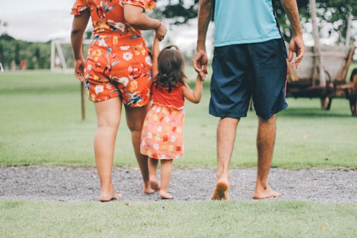 A close-up of a family walking barefoot on soft grass, sunlight filtering through trees, showing natural joyful movement.