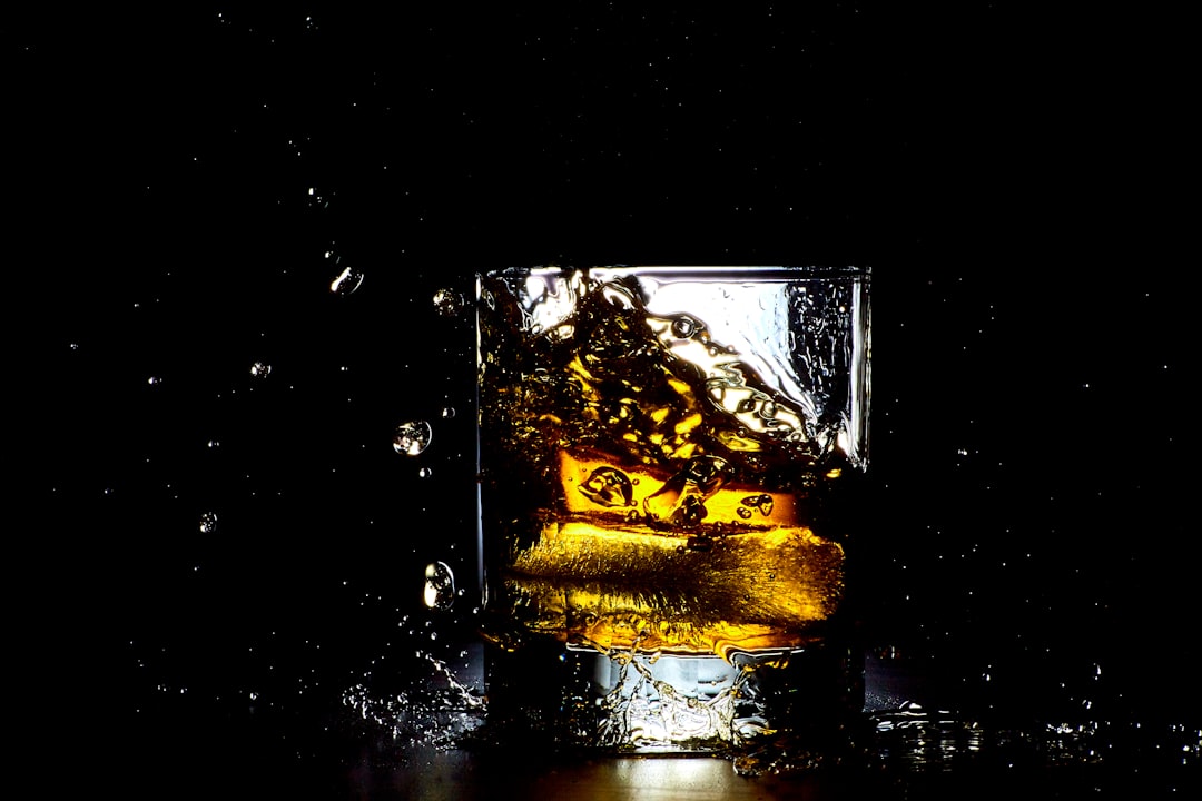 clear shot glass with ice and liquid, Ice splashing while falling into a glass of whiskey.
