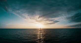A serene image of a lone sailboat gliding across calm blue waters under a golden sunset.