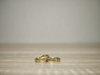 Elegant gold rings stacked together, reflecting warm light on a minimalist grey surface.