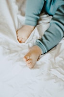 A close-up view of a child's legs and feet wearing light blue pajamas on a soft, white crumpled fabric background.
