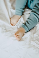 A close-up view of a child's legs and feet wearing light blue pajamas on a soft, white crumpled fabric background.