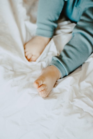 A close-up view of a child's legs and feet wearing light blue pajamas on a soft, white crumpled fabric background.