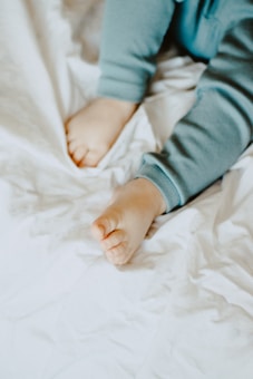 A close-up view of a child's legs and feet wearing light blue pajamas on a soft, white crumpled fabric background.