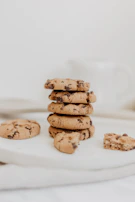 Warm, golden-brown chocolate chip cookies stacked beside a steaming cup of coffee on a cream linen cloth.