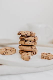 A stack of classic New York-style cookies with chocolate chips, placed next to a steaming cup of coffee on a cozy kitchen counter.