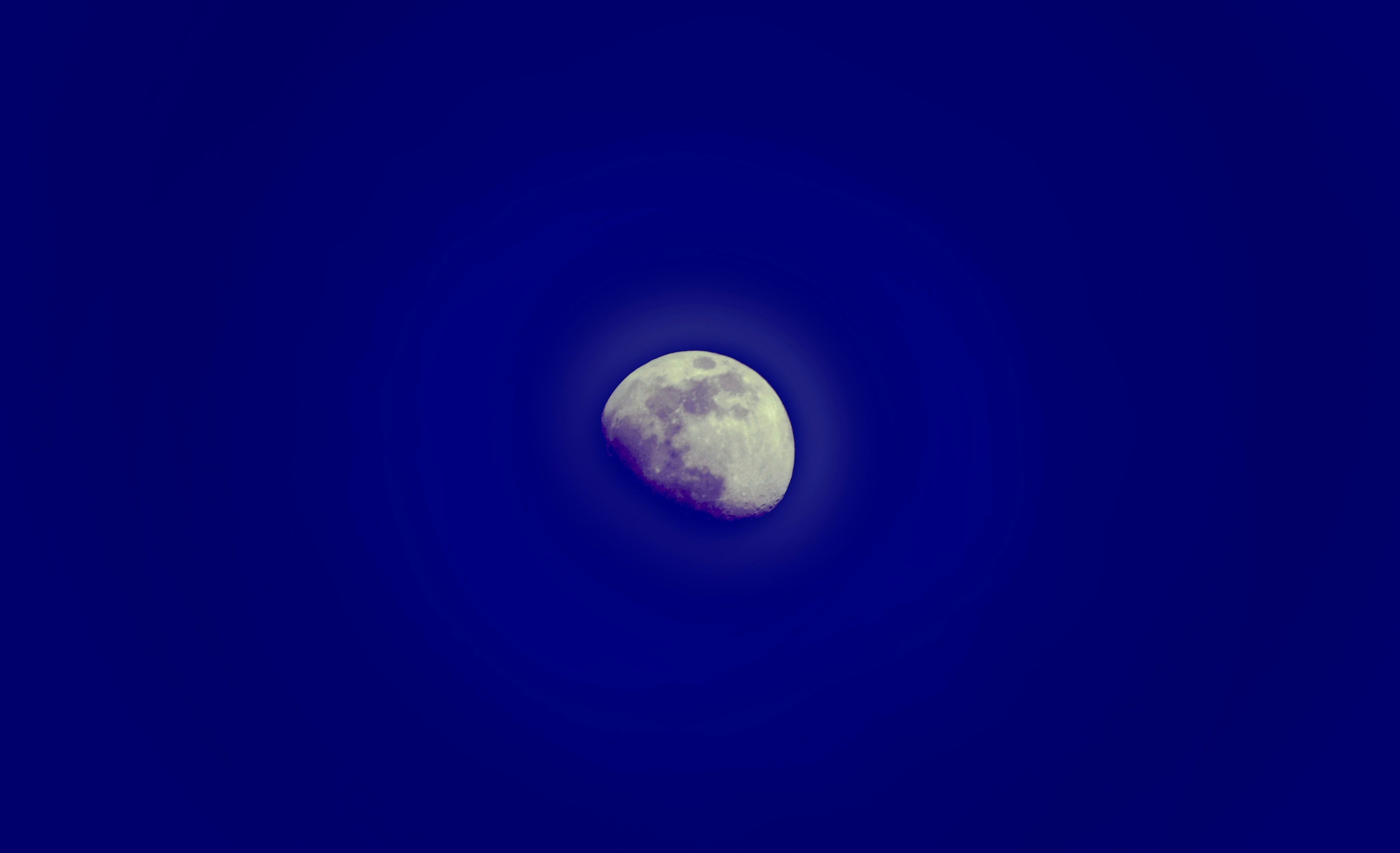A group of people, including families and friends, gathered in an open area at night, looking up at the sky with binoculars and small telescopes, excitedly pointing towards a reddish moon.