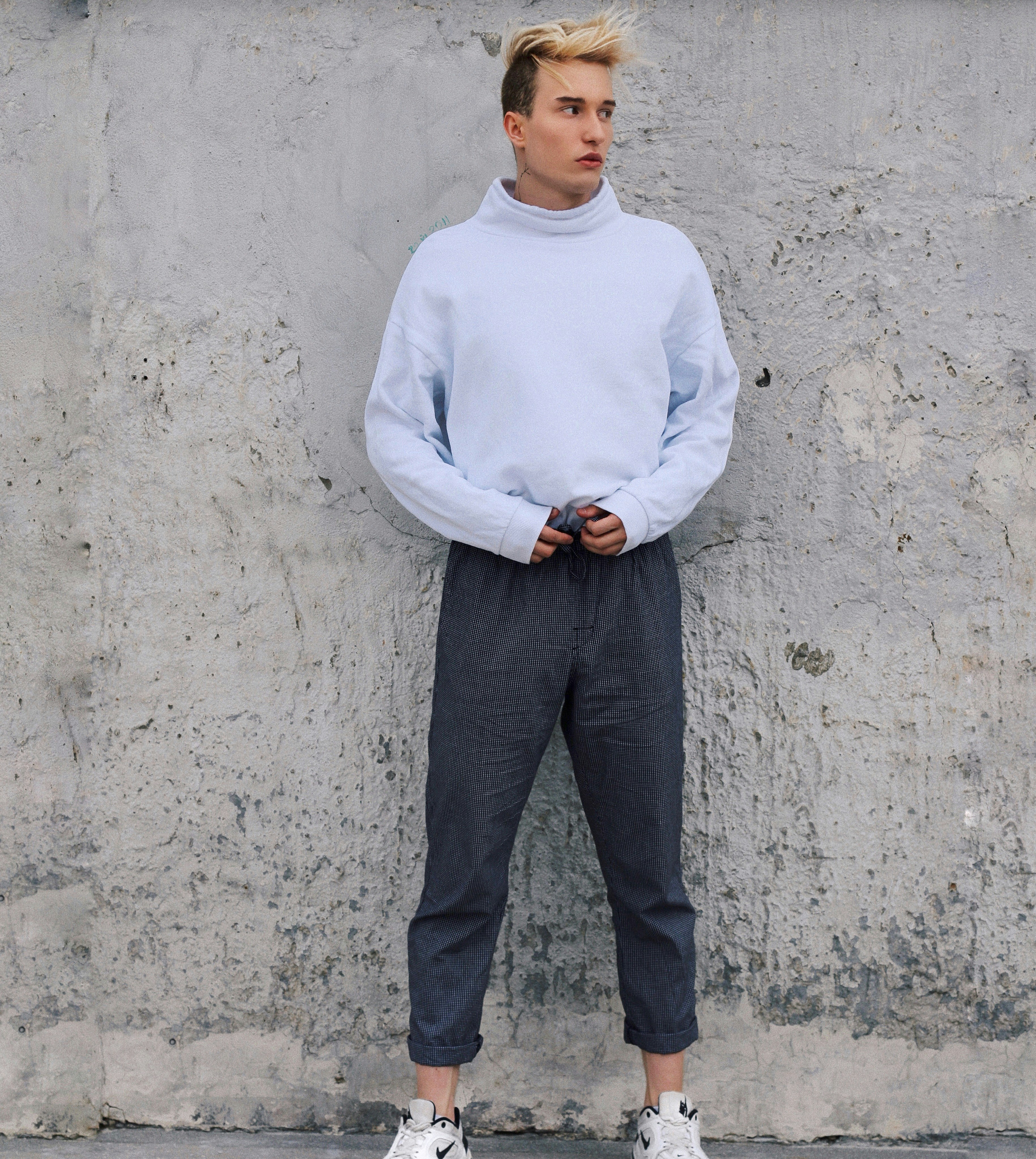 Man in white sweater standing in front of white concrete wall photo