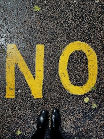 Close-up of a hand writing the word ‘No’ in bold letters on a notepad.