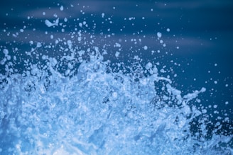 Dynamic spray of water captured in mid-air with droplets splashing against a deep blue background. The scene is vibrant and full of energy, showcasing the fluid motion of water.