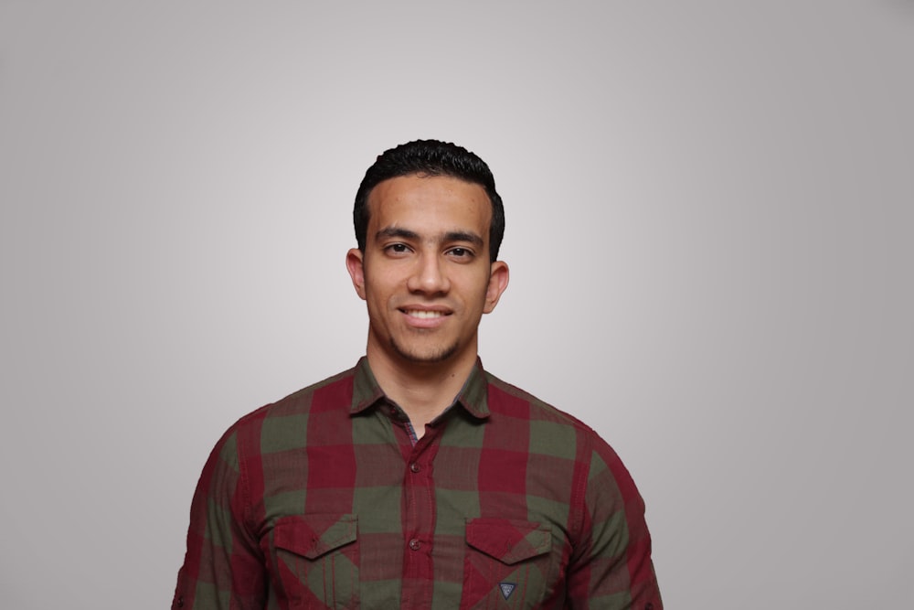 man wearing red and gray checked collared button-up long-sleeved shirt smiling and looking straight