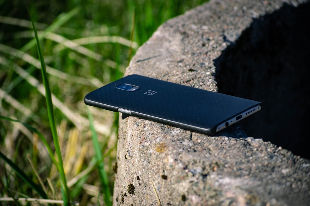 smartphone Android preto no pavimento de pedra cinza perto de gramíneas verdes