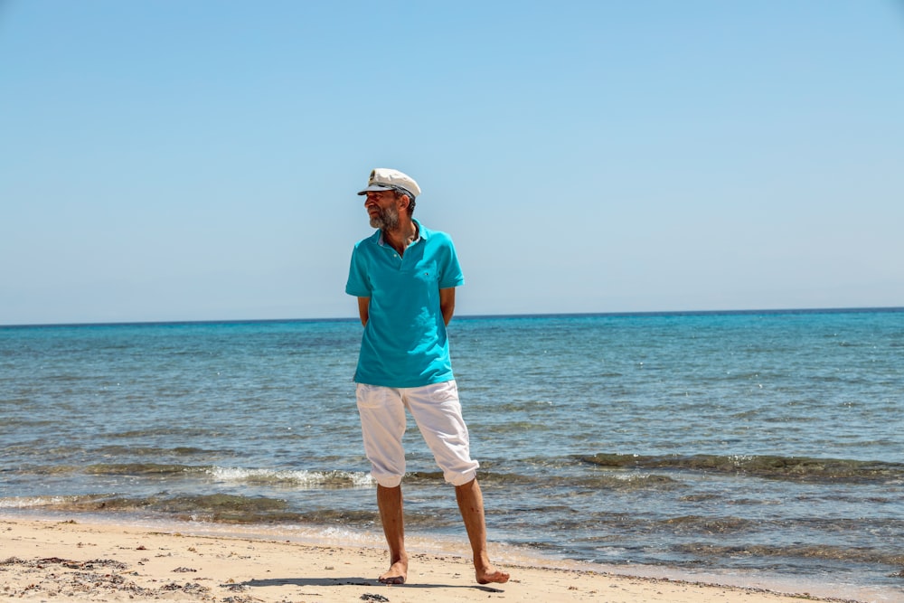 hombre vestido con polo azul y pantalones cortos blancos de pie en la orilla del mar durante el día