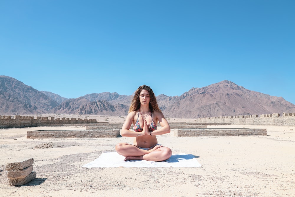 mujer con dos piezas meditando bajo el cielo azul durante el día