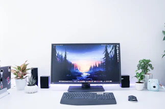 A clean, minimal desk setup with a laptop, notepad, and a simple plant beside a large window.