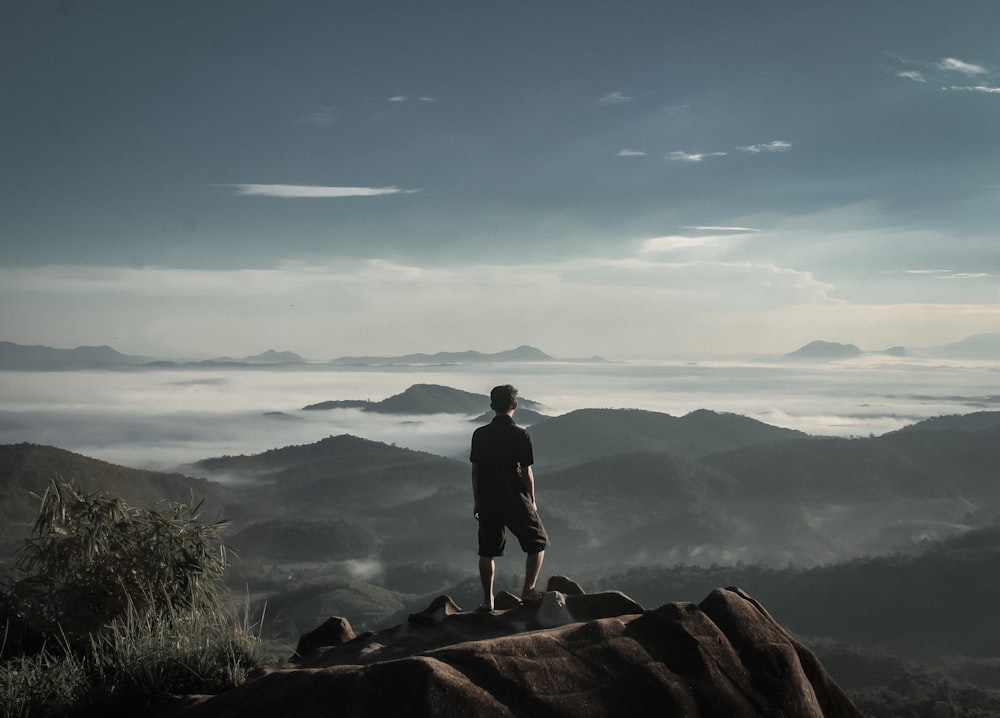 man standing on grey rock under grey sky