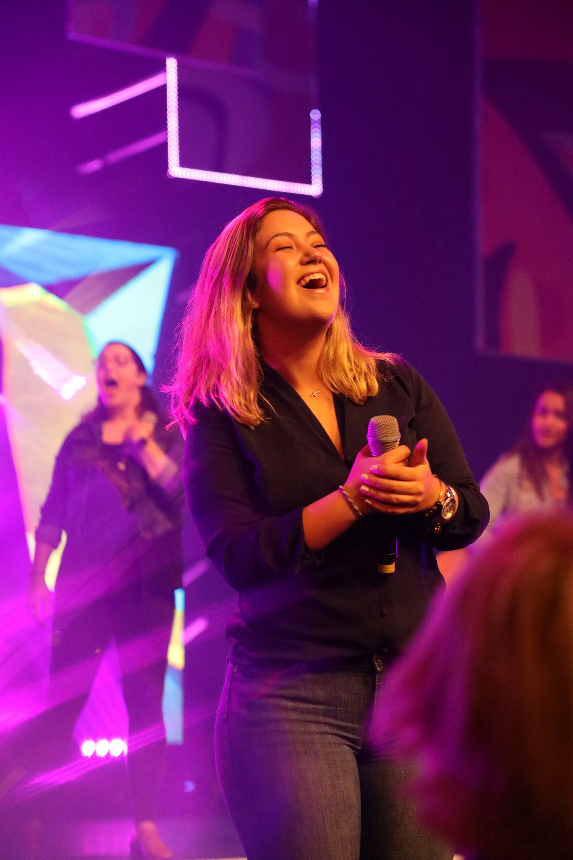 A dynamic shot of Luciana holding a microphone, her expression full of strength and joy, with a splash of colorful abstract art in the background.