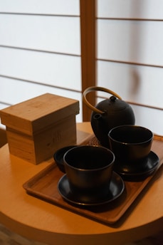 A traditional Japanese tea ceremony set with delicate porcelain cups and a rustic wooden table beside a paper screen.
