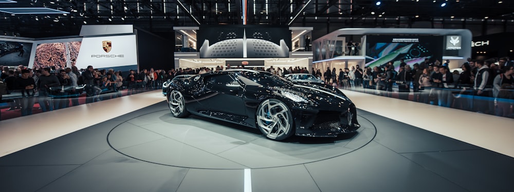 black Lamborghini on display surrounded with people watching