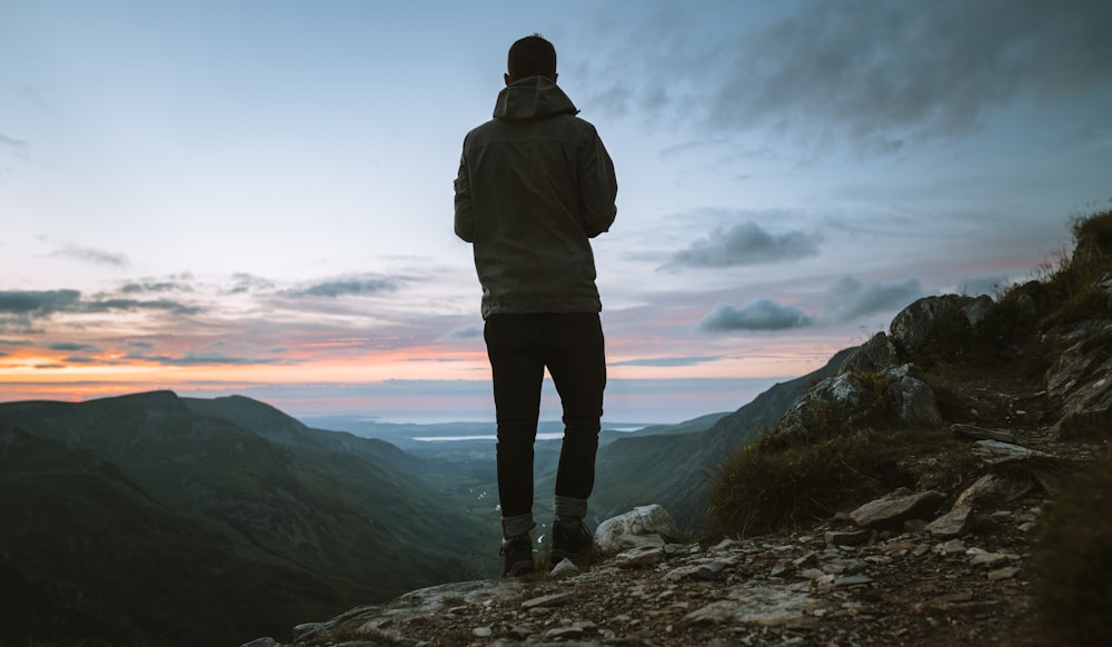 man in grey hoodie standing on cliff during sunrise