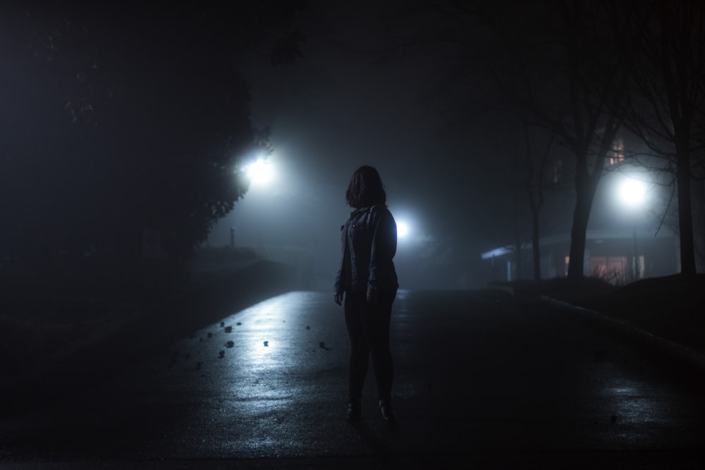 mulher na jaqueta em pé na estrada durante a noite