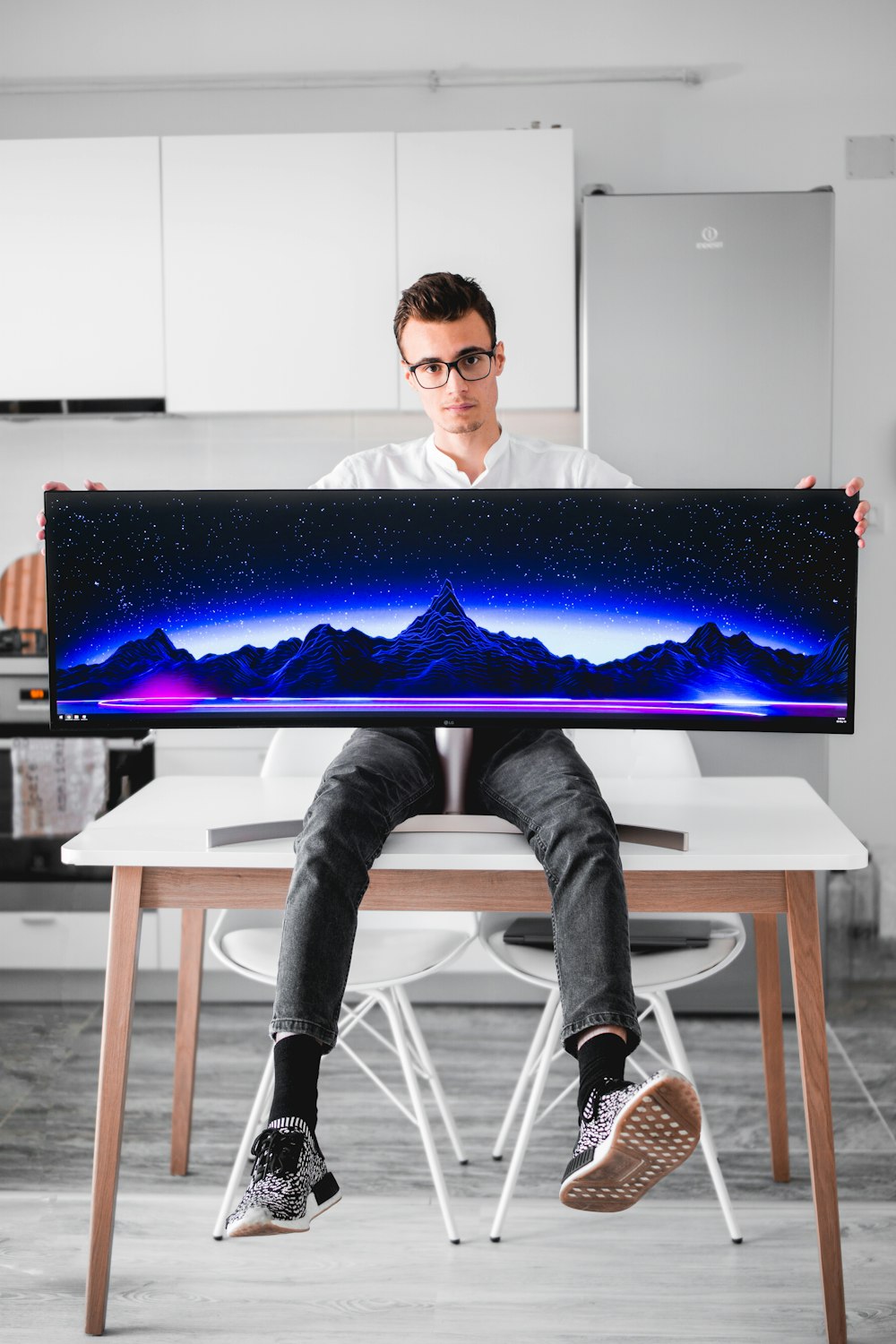 hombre sentado en la mesa sosteniendo un monitor de computadora de pantalla plana